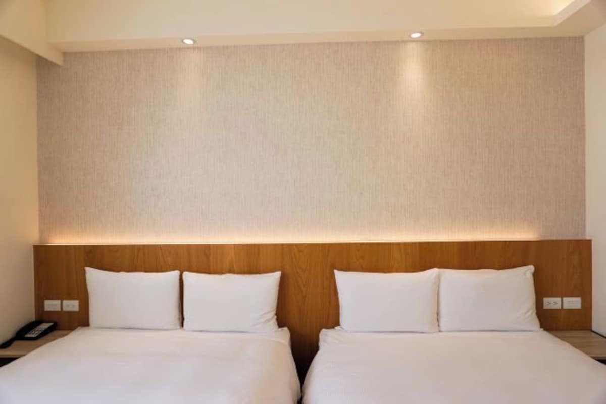 Una habitación de hotel con dos camas, un cabecero de madera y una pared de color neutro.