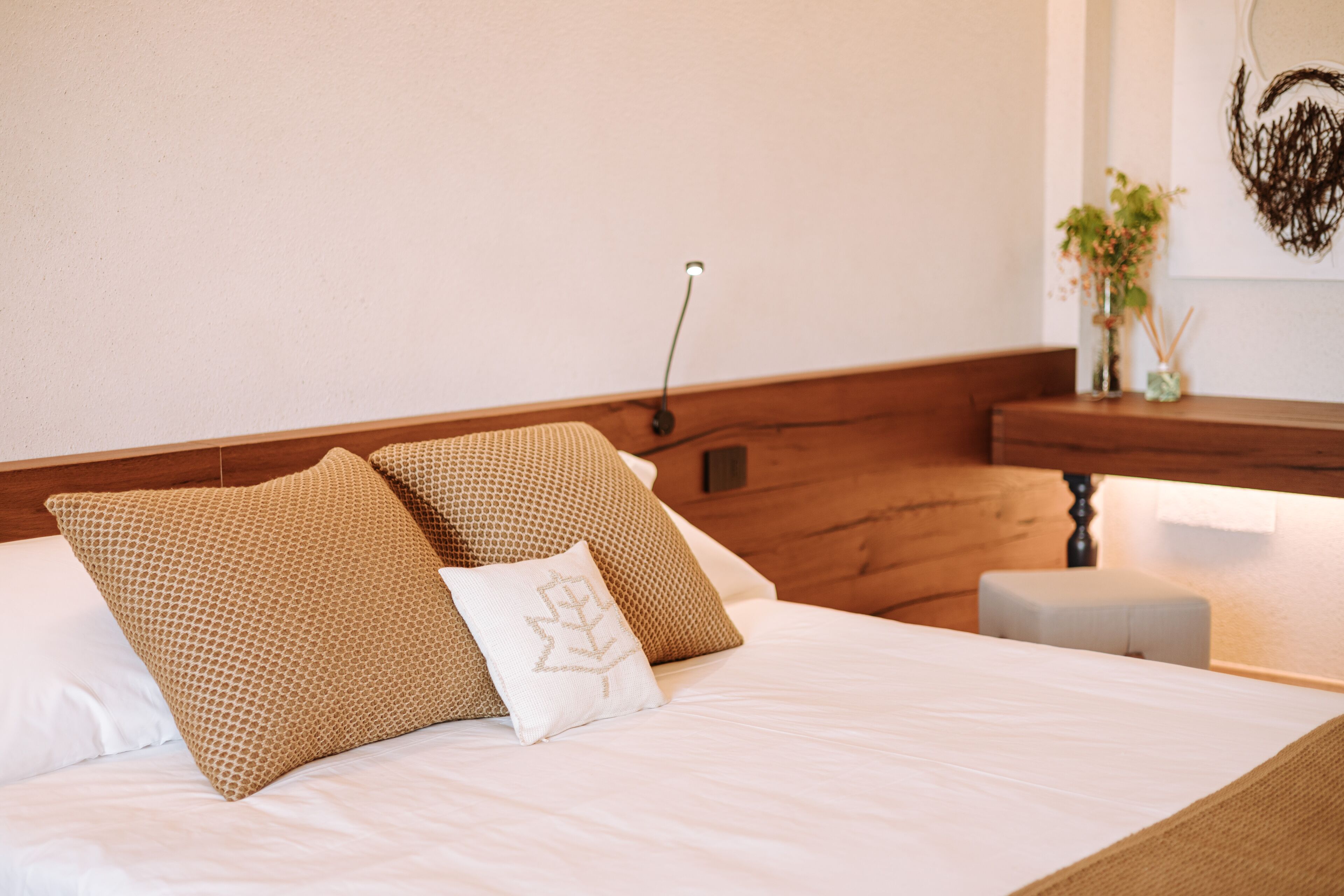 A neatly made bed with two patterned pillows and a white pillow with a leaf design.