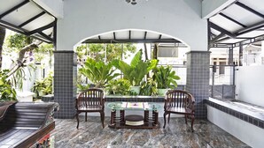 A covered patio area with a glass-top table, two wooden chairs, and a bench. - OYO 91868 Nusa Indah Guest House Syariah (Lamongan)