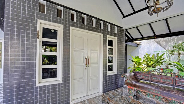 A room with a tiled wall, a white door, and a bench with decorative railings. - OYO 91868 Nusa Indah Guest House Syariah (Lamongan)