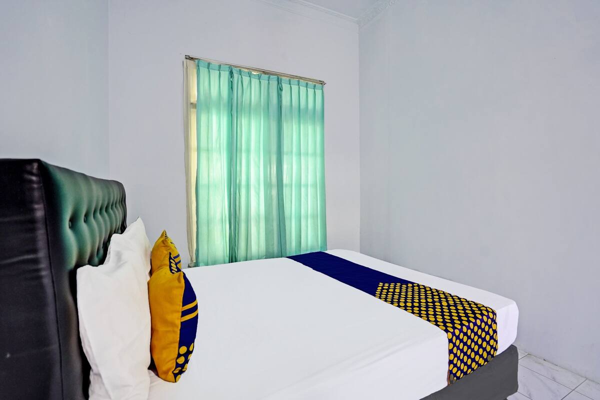 Une chambre d’hôtel avec un lit, une fenêtre avec des rideaux, un oreiller et une couvre-lit.