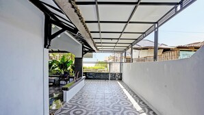 A covered outdoor area with patterned flooring, a seating area with tables and chairs, and a view of the surrounding neighborhood. - OYO 91868 Nusa Indah Guest House Syariah (Lamongan)