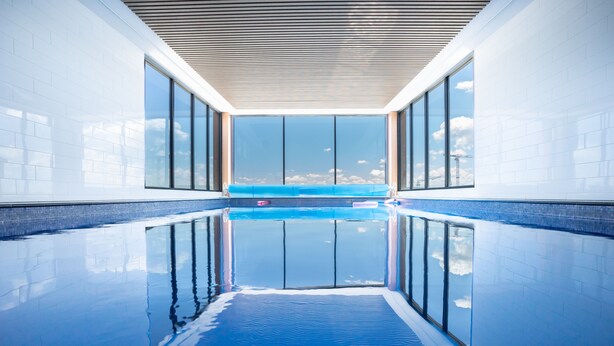 A modern indoor swimming pool with clear glass walls and a view of the sky. - Luxury Apartment in Dickson, Canberra (Dickson)