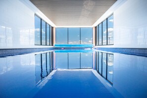 A modern indoor swimming pool with clear glass walls and a view of the sky. - Luxury Apartment in Dickson, Canberra (Dickson)
