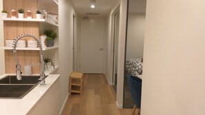 A narrow hallway with a kitchen area on the left, featuring a sink, shelves with jars, and a small wooden stool. - Luxury Apartment in Dickson, Canberra (Dickson)