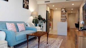 A modern living room with a blue sofa, a wooden coffee table, and a kitchen area in the background. - Luxury Apartment in Dickson, Canberra (Dickson)