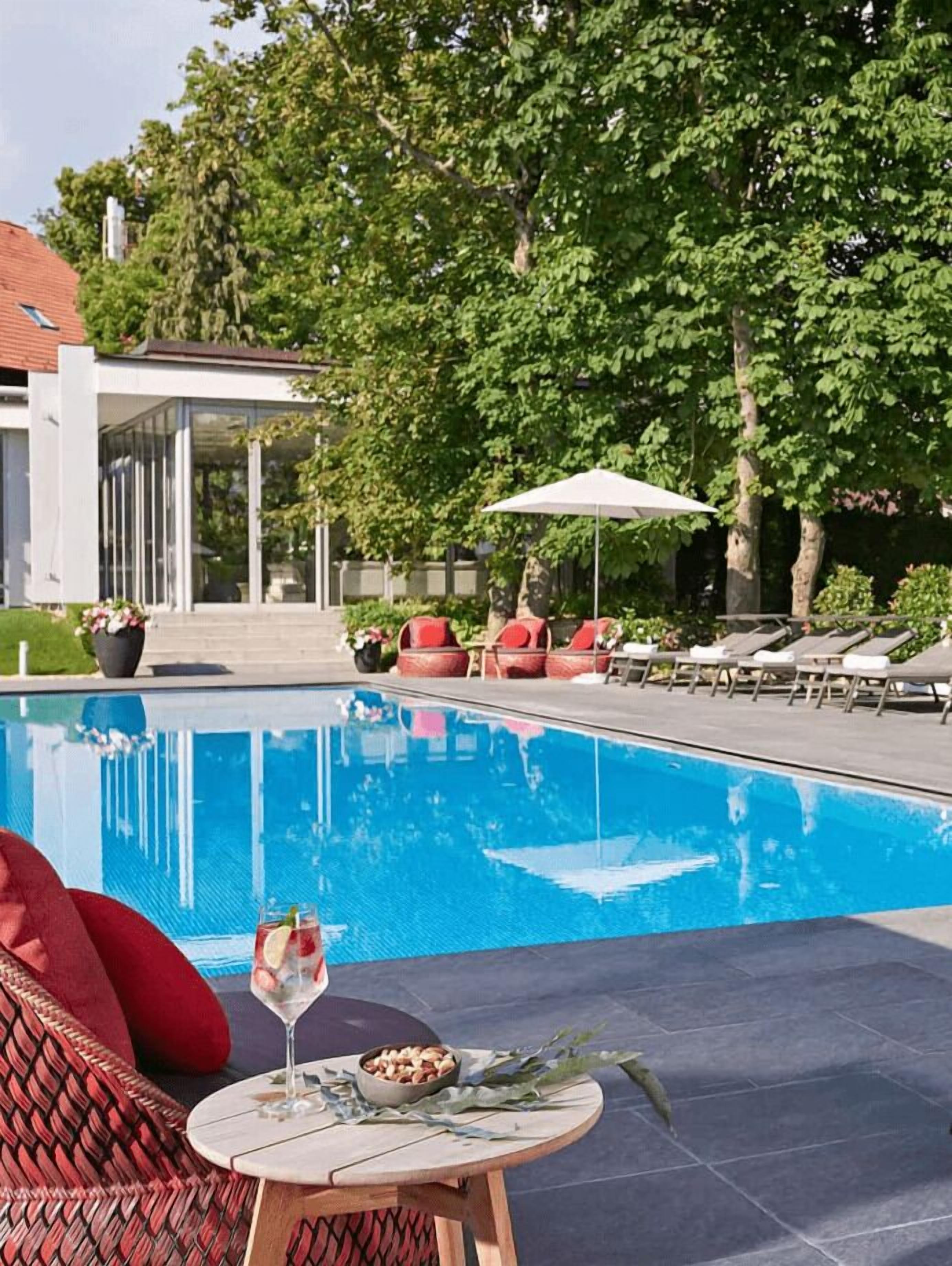 A swimming pool with lounge chairs and a table with a drink and snacks.