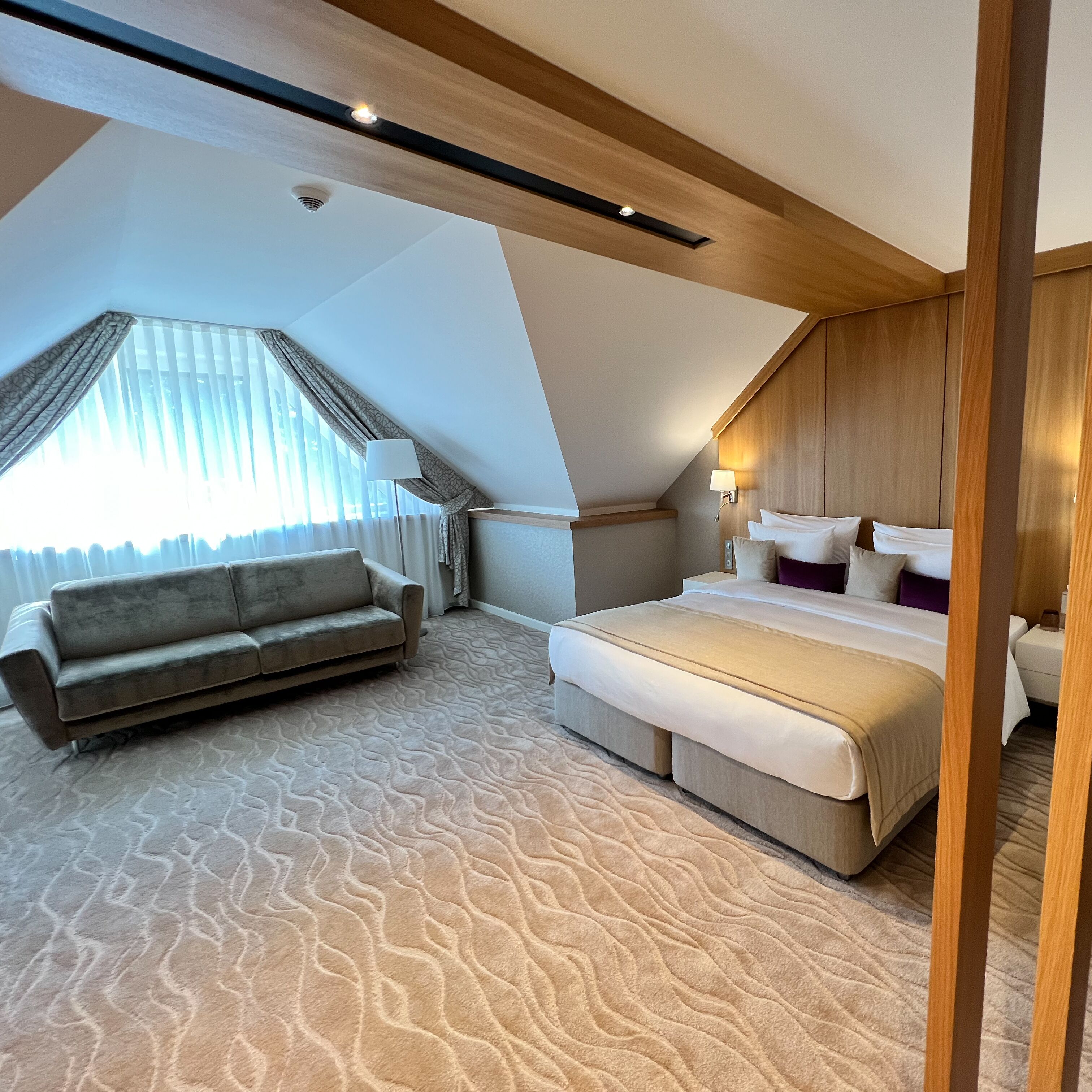 A modern bedroom with a large bed, a sofa, and a ceiling with exposed beams.