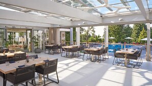 A spacious outdoor dining area with tables and chairs, a pool, and a glass ceiling structure. - Normafa Hotel (Budapest)