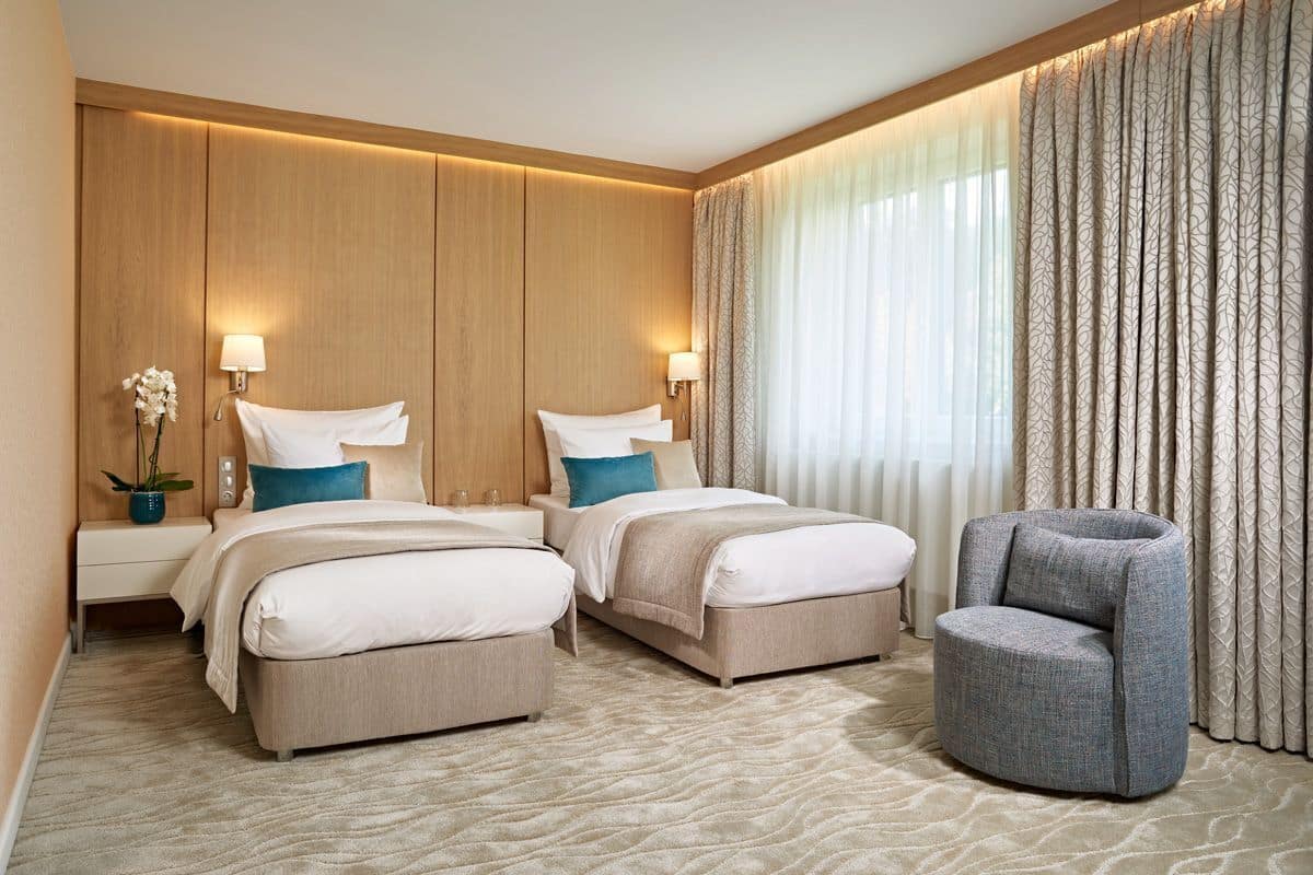 Habitación de hotel con dos camas, una zona de estar y un amplio ventanal con cortinas.