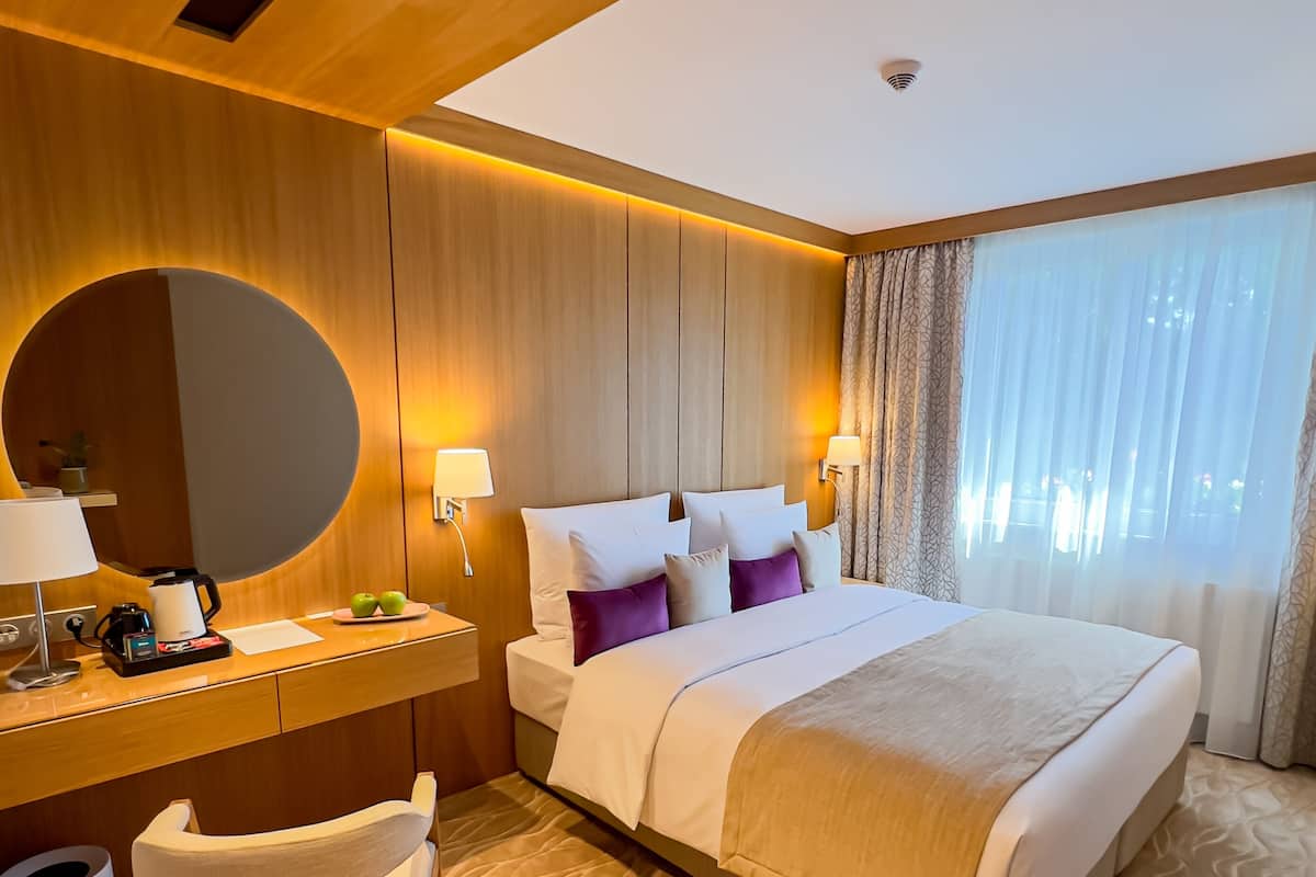 Habitación de hotel con una cama grande, un escritorio con lámpara, una silla y un espejo redondo.