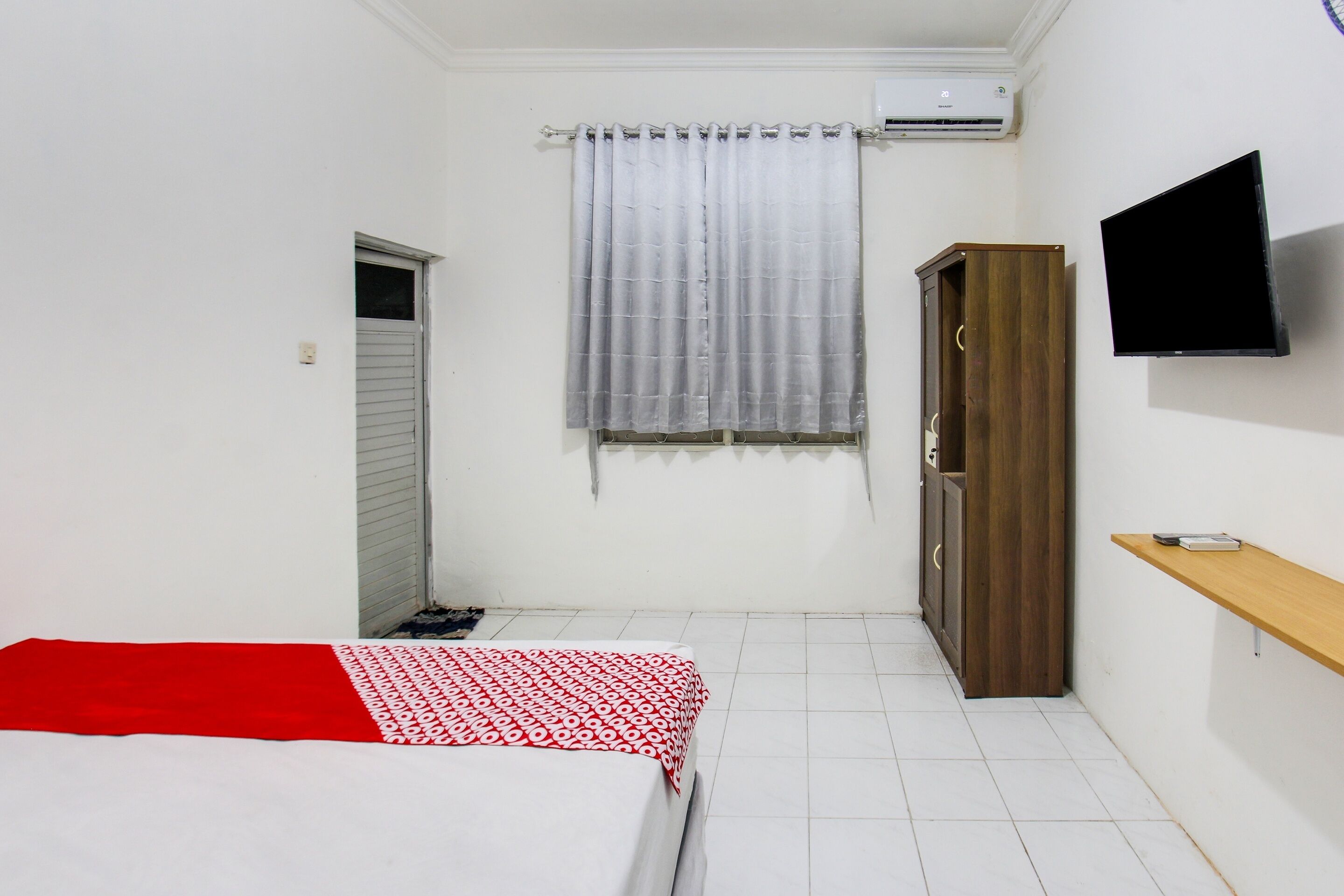 A small, clean room with a bed, a TV, a wardrobe, and a window with curtains.