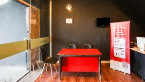 A conference room with a red table, black chairs, a glass partition, a clock, a framed certificate, and a promotional stand. - OYO 91391 Mutiara Syariah 3  (Mataram)