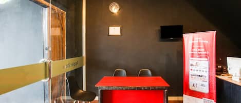 A conference room with a red table, black chairs, a glass partition, a clock, a framed certificate, and a promotional stand.