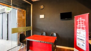 A conference room with a red table, black chairs, a clock, a framed certificate, and a TV on the wall. - OYO 91391 Mutiara Syariah 3  (Mataram)