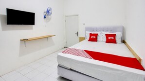 A hotel room with a bed, a TV mounted on the wall, a bedside table, and a door. - OYO 91391 Mutiara Syariah 3  (Mataram)