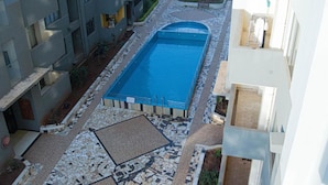 Et rektangulært swimmingpool med flisebelagt areal, omgivet af en lav mur og et lille haveområde.