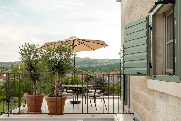 Un balcón con mesa y sillas, un árbol en maceta y vistas del paisaje circundante.