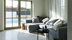 A living room with a grey sofa, a small side table, and a view of a swimming pool through a glass door. - Villa Mara Casa Rustica ZadarVillas (Korcula)