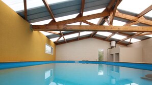 An indoor swimming pool with a wooden ceiling and walls, a blue pool floor, and a door leading to another room. - Spacious house with heated pool and pets allowed (Vesly)