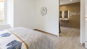 A modern bedroom with a large bed, a decorative wall piece, and a view into a bathroom with a modern sink and mirror. - Spacious house with heated pool and pets allowed (Vesly)