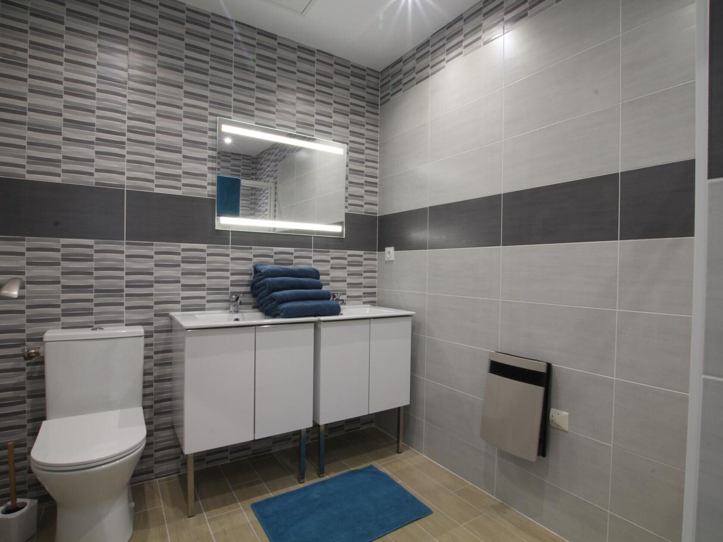 Un baño moderno con inodoro, lavamanos con espejo y un perchero para toallas.