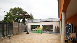 A wooden deck with a table and chairs, a green trash bin, and a metal fence. - Spacious house with heated pool and pets allowed (Vesly)
