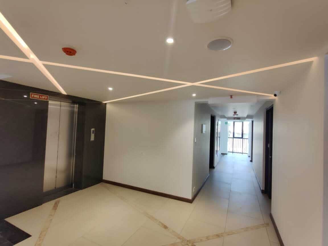 A spacious hallway with a fire lift, a tiled floor, and a ceiling with recessed lighting and a smoke detector.