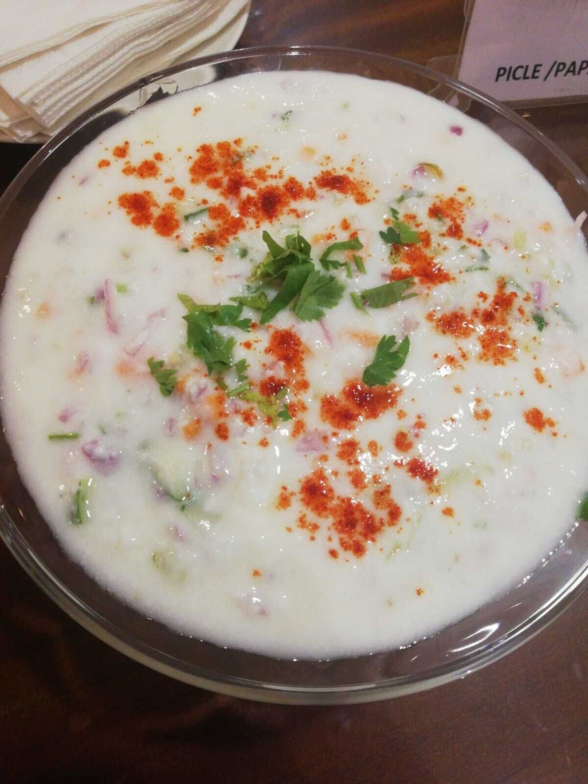 A bowl of white soup with red spices and green herbs.