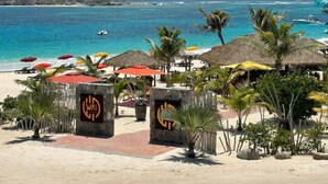 Ein Hotel am Strand mit strohgedeckten Hütten, Palmen und Strandsonnenschirmen.