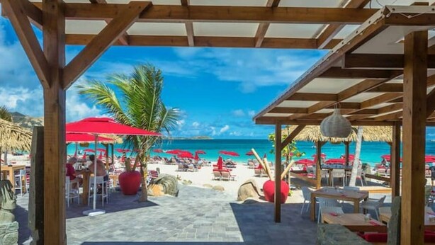 Ein Restaurant direkt am Strand mit Terrassensitzplätzen, Palmen und Meerblick.
