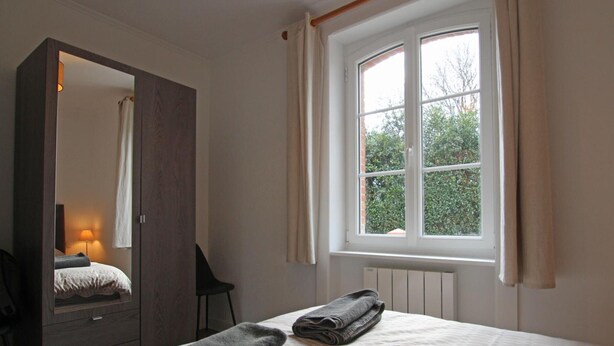 Ein Schlafzimmer mit großem Kleiderschrank, einem Bett mit gemustertem Überwurf und einem Fenster mit Vorhängen.