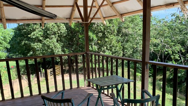 Terraza exterior con mesa y sillas, rodeada por una barandilla de madera, con vistas a un jardín.