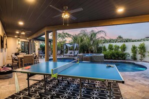 Mesa de ping pong con red, piscina, asientos al aire libre y ventilador de techo.
