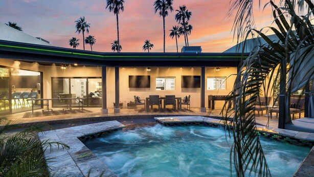 Una casa moderna con piscina, mobiliario exterior y palmeras.