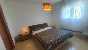 Ein Schlafzimmer mit einem Bett, einem Nachttisch, einer Lampe, einem Fenster mit Vorhängen und einer Tür.