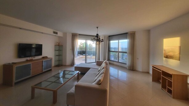 Ein geräumiges Wohnzimmer mit Sofa, Couchtisch, Fernseher und einem Balkon mit Blick.