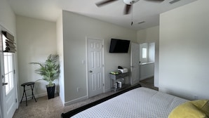 A bedroom with a bed, a ceiling fan, a TV, a desk, and a potted plant. - Experience Downtown Charm and Modern Comfort at  Your Perfect VRBO Getaway! (Pensacola)