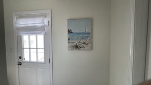 A door with a white frame and a window, a white door mat, and a painting of a sailboat on a dock. - Experience Downtown Charm and Modern Comfort at  Your Perfect VRBO Getaway! (Pensacola)