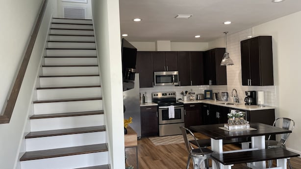 A modern kitchen with dark cabinets, stainless steel appliances, and a wooden dining table. - Experience Downtown Charm and Modern Comfort at  Your Perfect VRBO Getaway! (Pensacola)