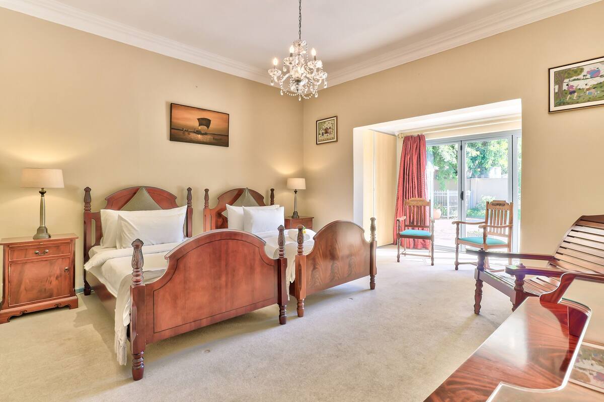 A bedroom with a wooden bed, bedside tables, a chandelier, and a view of the outdoors.
