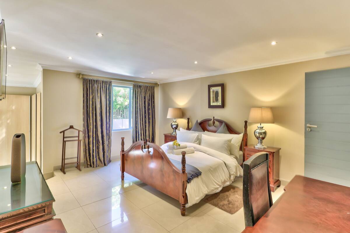 A bedroom with a bed, bedside tables, a nightstand, a chair, a lamp, and a window with curtains.