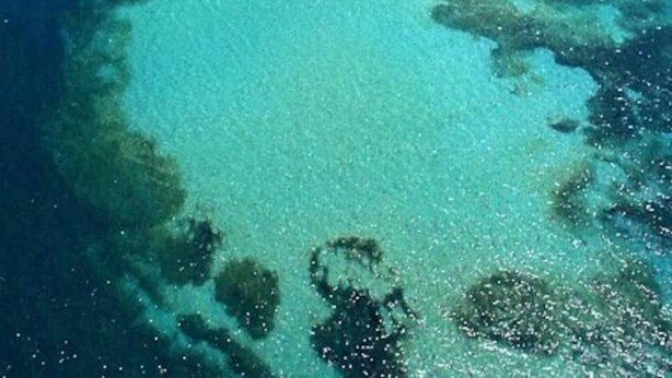 Vista aerea di una zona costiera con acque cristalline turchesi, una spiaggia sabbiosa e imbarcazioni.