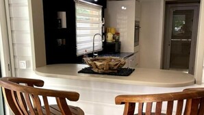 Una cucina moderna con un piano di lavoro bianco, due sgabelli da bar in legno e uno schienale nero.