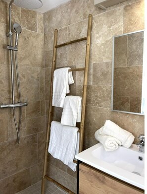 A bathroom with a shower, a wooden towel rack, and a sink.