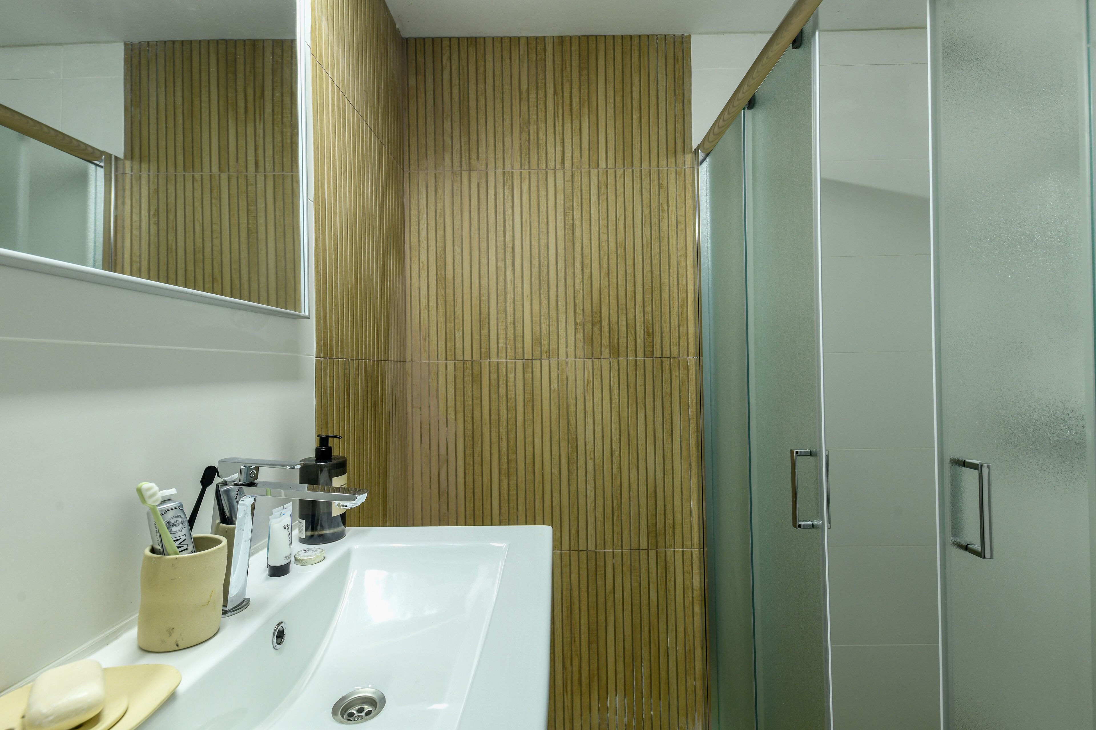 A modern bathroom with a white sink, a mirror, and a wooden panel wall.
