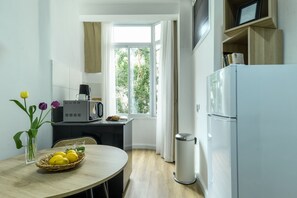A compact kitchen with a dining table, a microwave, a refrigerator, and a window with a view of greenery. - Charming Studio Apartment with kitchen (Tel Aviv)