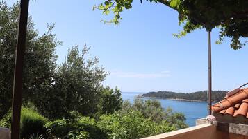 Une terrasse avec vue sur la mer, entourée de verdure et surmontée d’un toit en tuiles.