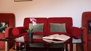 A red sofa with green cushions, a black coffee table, and a potted orchid. - Apartment Lile (Dubrovnik)