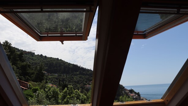 A room with a skylight overlooking a coastal landscape with trees and buildings. - Apartment Lile (Dubrovnik)